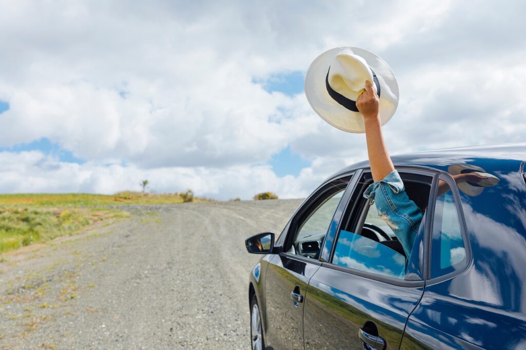 woman holding hat out of car window